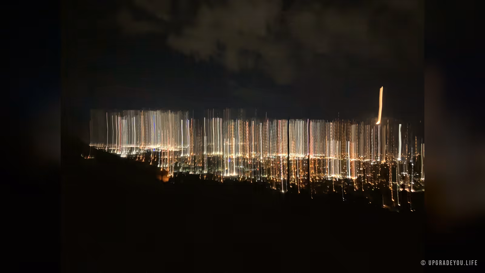Warm city lights glowing in long streaks across a dark valley at night
