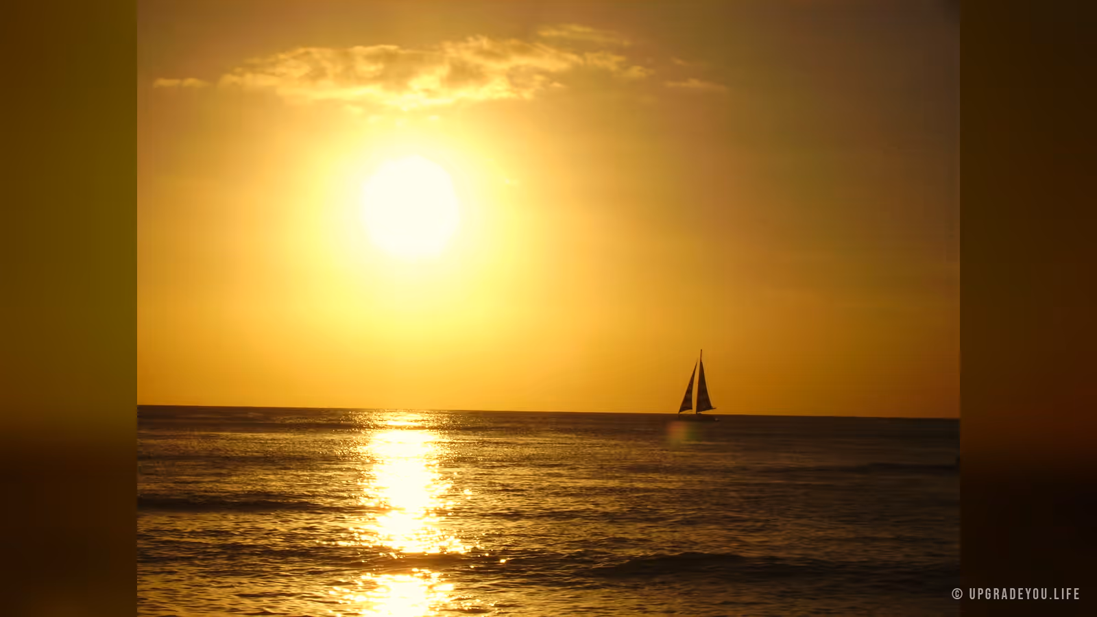 A lone sailboat on a vast golden sea at sunset