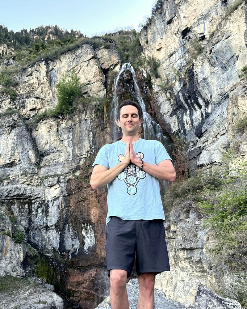Jess in piedi ai piedi di una cascata, i palmi uniti al petto, gli occhi chiusi.